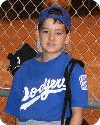 Boy in blue baseball uniform by fence.